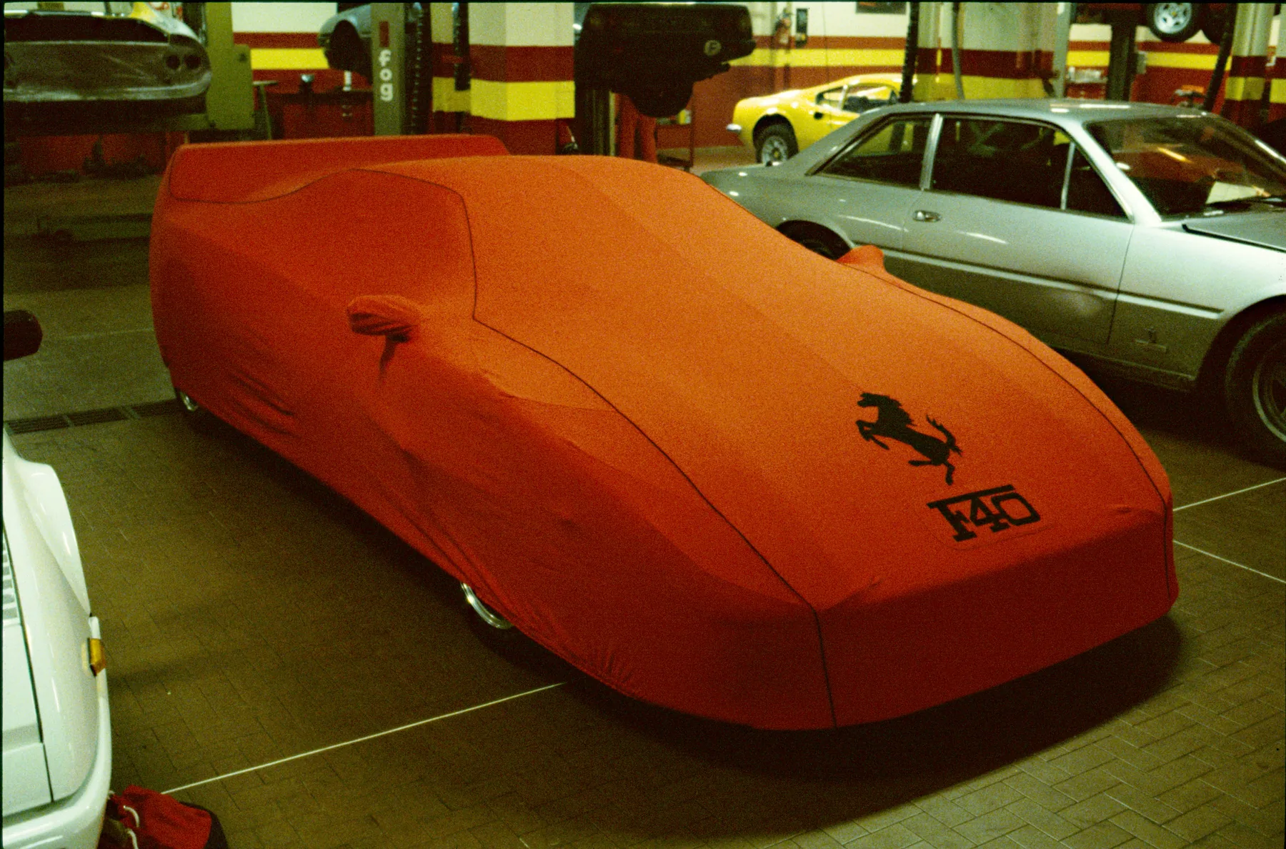 Ferrari F40 sous housse intérieure rouge, cavallino et sigle F40 brodés, dans l'atelier