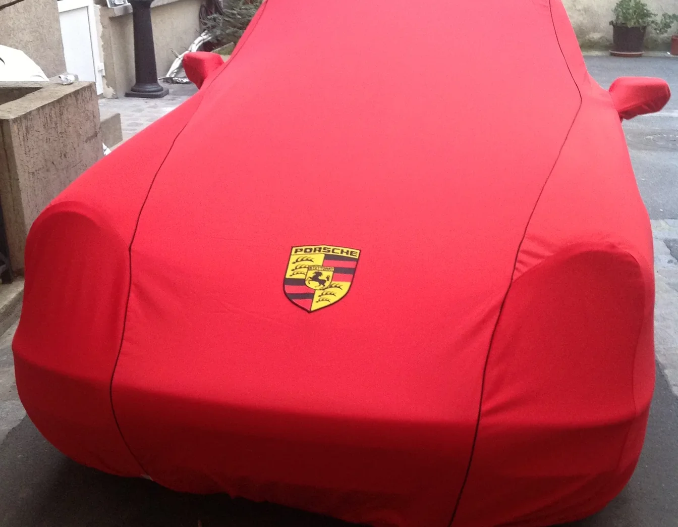 Porsche couverte d'une housse rouge ajustée, écusson Porsche brodé sur le capot et poches de rétroviseurs