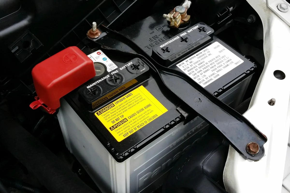 Batterie de voiture ouverte dans son compartiment, avec ses deux bornes et sa cosse rouge