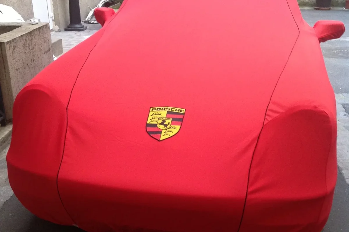 Avant d'une voiture sous une housse rouge sur mesure, avec écusson brodé et poches pour les rétroviseurs