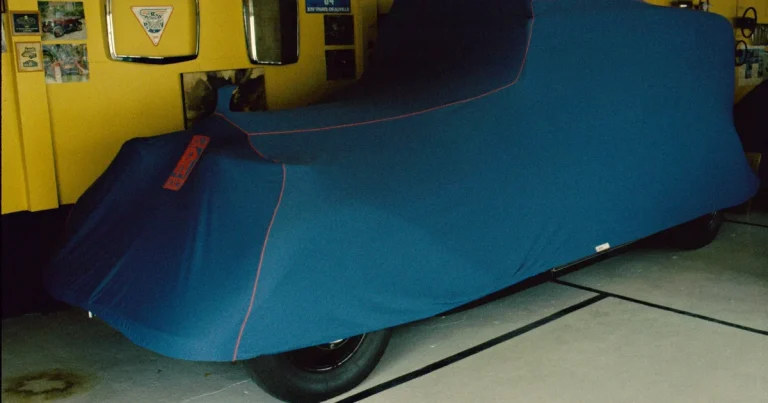 Voiture ancienne sous une housse bleue à passepoil rouge, garée dans un garage aux murs jaunes