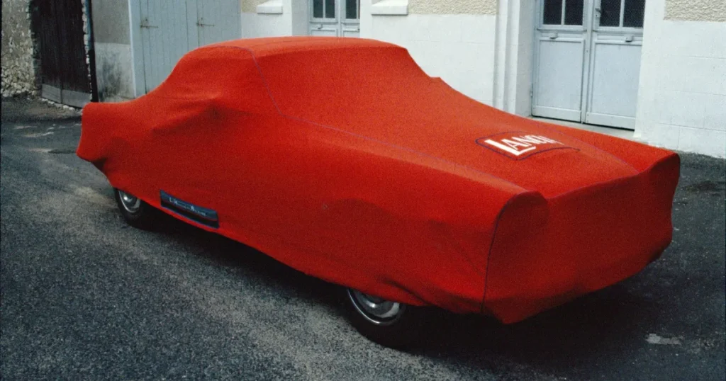 Voiture ancienne rouge recouverte d'une housse ajustée, cousue à l'atelier, qui épouse les ailes et le coffre
